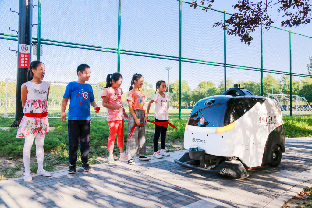 Idriverplus WOXIAOBAI, equipped with two Velodyne Puck sensors, safely navigates and cleans streets in China with children looking on